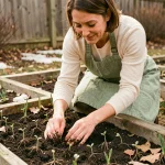Femme préparant des plantations printanières dans un jardin résidentiel, pressant des jeunes plants dans une terre humide et sombre au début du printemps