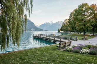 Vue panoramique du Lac d'Annecy depuis un parc public avec passerelle en bois et montagnes enneigées en arrière-plan